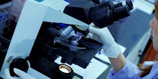 在实验室里透过显微镜看东西的女科学家