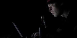 一个在黑暗中看着电脑显示器的惊讶男子的侧面视图