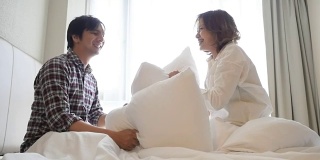 一对年轻夫妇在床上用枕头吵架