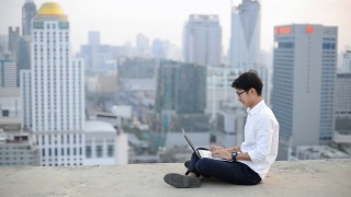 年轻的商人使用笔记本电脑，看城市景观，亚洲视频素材模板下载