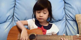 可爱的女孩在沙发上弹吉他尤克里里