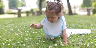 一个一岁的小女孩，在一个公园里长满鲜花的草地上学习爬行