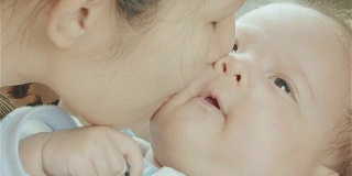 亚洲母亲抱着和亲吻她的混合种族可爱的小新生儿女孩的脸颊在她的卧室
