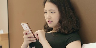 亚洲女性使用智能手机上的应用程序发送短信。漂亮的年轻女孩在酒店使用智能手机。