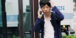 日本学生在电话亭旁边用手机