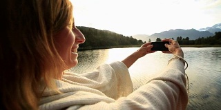 一名女子用手机拍摄山湖景观