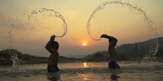 剪影快乐的孩子戏水在池塘在日落。