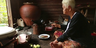 生活方式资深亚洲妇女坐在烹饪食物，慢动作