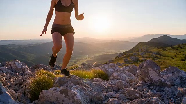 年轻的女性跑步者在日落时跑上山坡的岩石景观