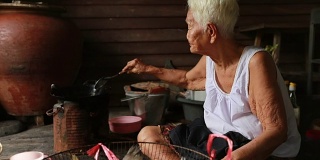生活方式资深亚洲妇女坐在烹饪食物，慢动作