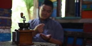 一名亚洲男子在古董屋检查咖啡豆的质量，然后将其放入咖啡研磨机。