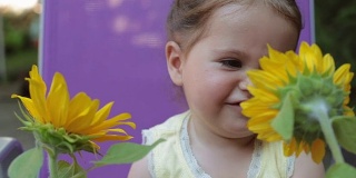 小女孩在后院和向日葵在户外玩耍的肖像——闻着香味，面带微笑