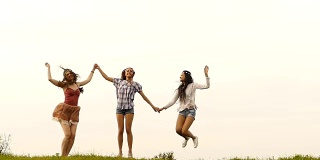 三个欢快的年轻女人手牵着手跳跃，慢镜头