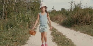 一个小女孩走在尘土飞扬的乡间小路上。真实的人，乡村景色，不寻常的角度。