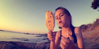 日落海滩上的小女孩吃冰淇淋，弄得一团糟。