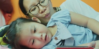 亚洲母亲和她的女儿在床上使用智能手机
