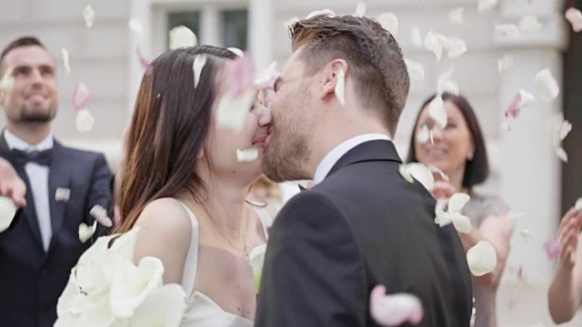 新婚夫妇亲吻，而婚礼上的客人扔花瓣