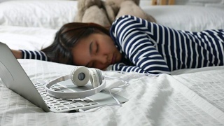 多莉用笔记本电脑拍摄了耳机，背景是一名正在睡觉的年轻女子视频素材模板下载