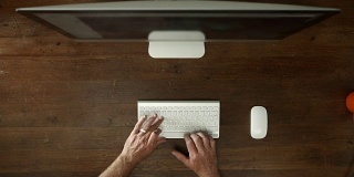 头顶的桌子上有台式电脑和男性的手打字