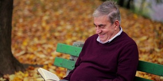 高级微笑男子在公园里看书