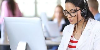 亚洲女性带着耳机和眼镜在工作场所使用电脑