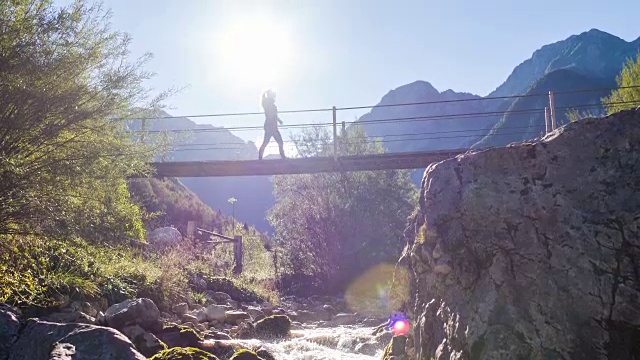 一名年轻女子正穿过山间溪流上的吊桥