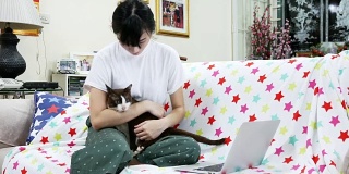 一位年轻女子在家里和一只猫一起用她的笔记本电脑