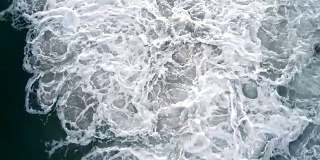 一个年轻人在暴风雨的海洋中游泳，被巨大的危险波浪击中。无人机视频正上方。