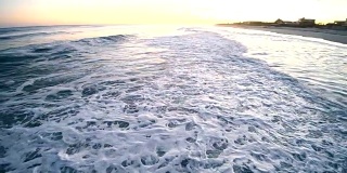 日落时分，一名年轻男子和一名少女在海里游泳，被海浪击中。汉普顿海滩，长岛，纽约州，美国。