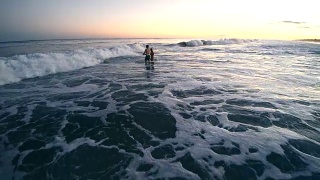 日落时分，一名年轻男子和一名少女在海里游泳，被海浪击中。汉普顿海滩，长岛，纽约州，美国。视频素材模板下载
