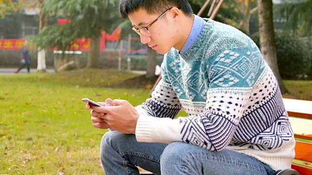 亚洲男子学生在公园拿着手机