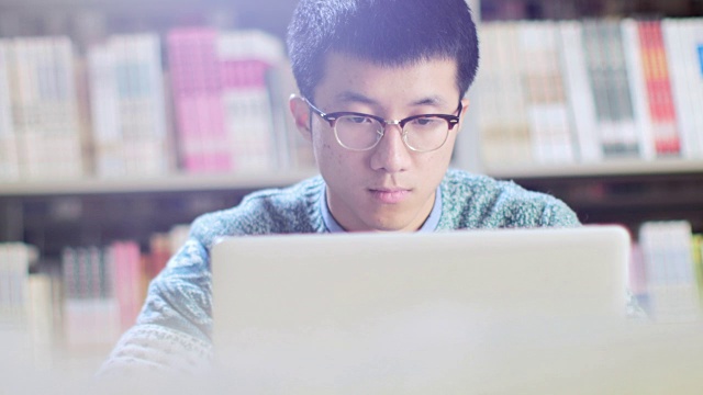 亚洲男学生在图书馆使用笔记本电脑