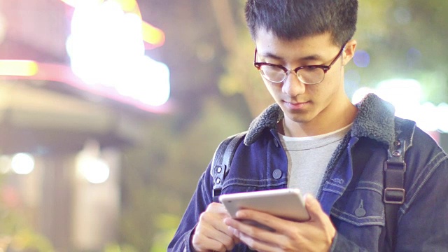 亚洲男子学生晚上在街上拿着手机