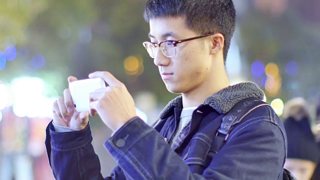 亚洲男子学生晚上在校园里拿着手机