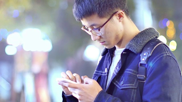 亚洲男子学生晚上在校园里拿着手机