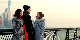 三个年轻的朋友，一个年轻的男子和两个十几岁的女孩，在曼哈顿市中心的synset广场前的海滨见面聊天