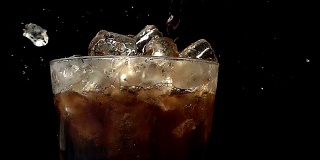 以慢动作将可乐苏打倒入装有冰块的黑色背景中