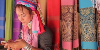 一名妇女穿着传统服装，拿着手机在村里织布