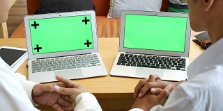 两人用绿屏笔记本电脑讨论