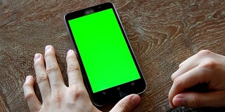 手用带有绿色屏幕的手机放在木桌上