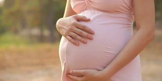 孕妇的手抚摸着她穿着粉色裙子的肚子