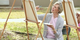 两个年长的女人一边在画布上画画一边聊天