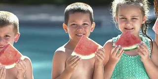 三个孩子夏天在泳池边吃西瓜