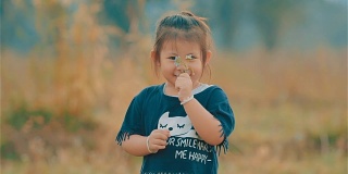 一个微笑的亚洲可爱女孩的肖像看着相机和闻到草地上的花