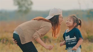 快乐的亚洲年轻母亲亲吻她的孩子的脸颊与模糊的田野一起视频素材模板下载