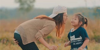 快乐的亚洲年轻母亲亲吻她的孩子的脸颊与模糊的田野一起