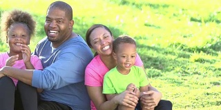 快乐的黑人家庭和两个孩子坐在草地上