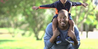 一个非裔美国小男孩在爸爸的肩膀上玩耍