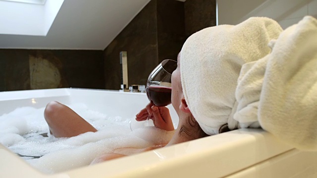 放松的女人在浴缸里喝葡萄酒