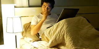 亚洲人电脑程序员工作到很晚，在卧室里使用笔记本电脑